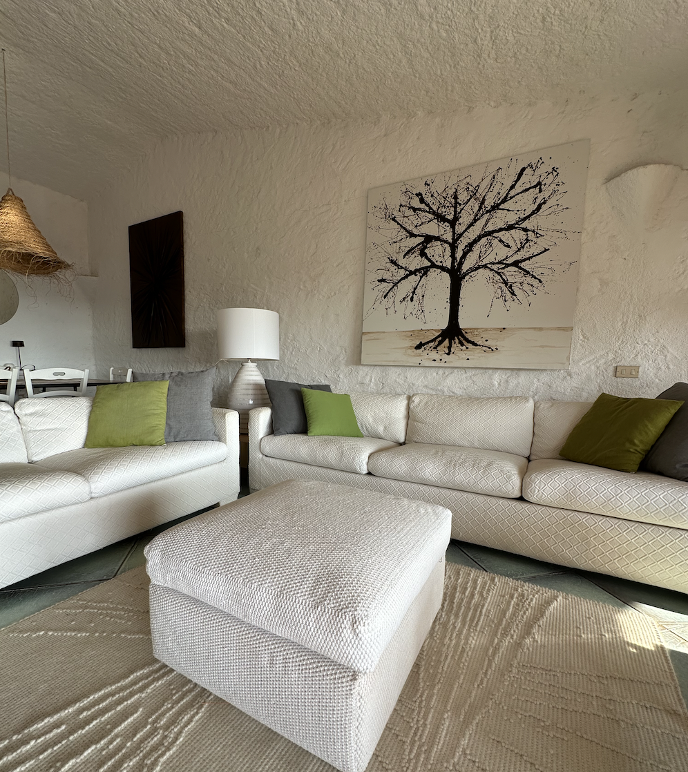 Modern living room with a beige sectional sofa, ottoman, and decorative tree wall art.